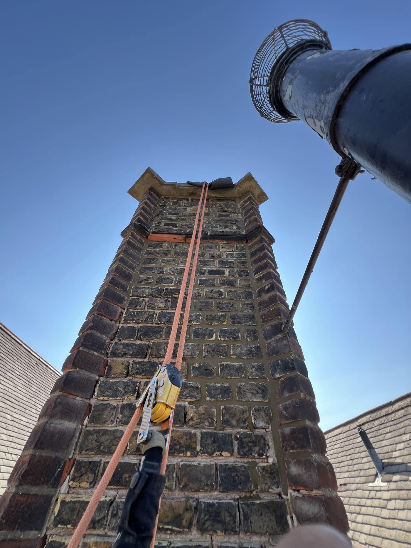 Rope lines rigged to a brick chimney stack against a clear sky