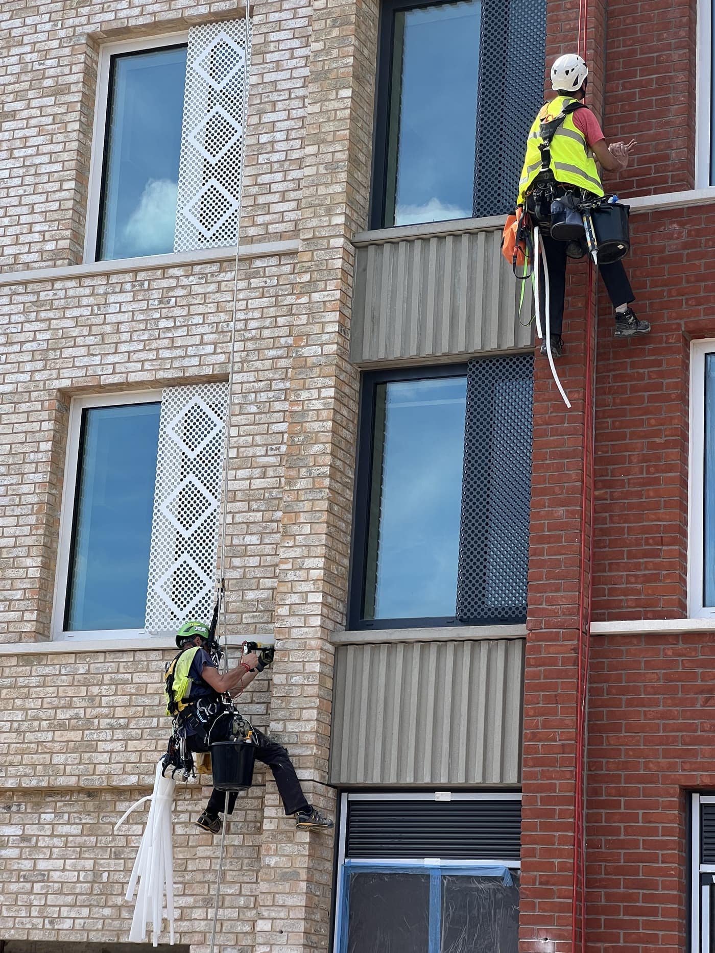 A BOVI Access technician on rope applying sealant from a cordless gun into a vertical joint in a brick elevation
